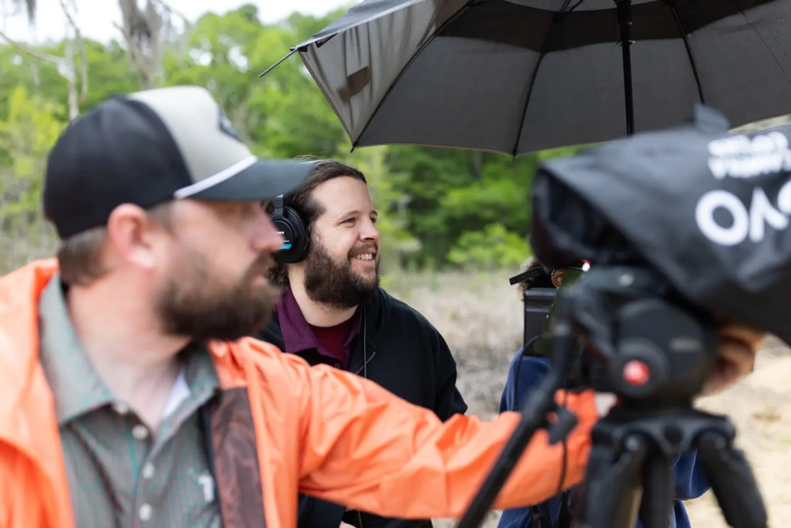 Crew filming an outdoor interview under an umbrella